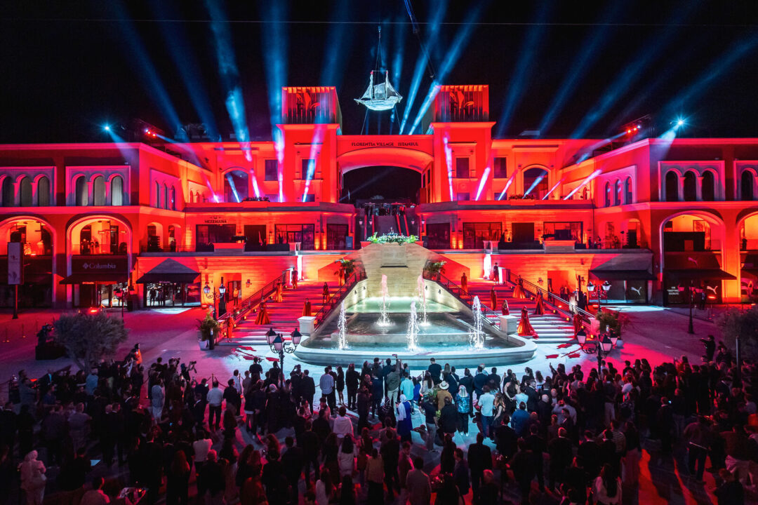 Florentia Village Istanbul façade lit red, with a suspended galleon and light beams above the crowd
